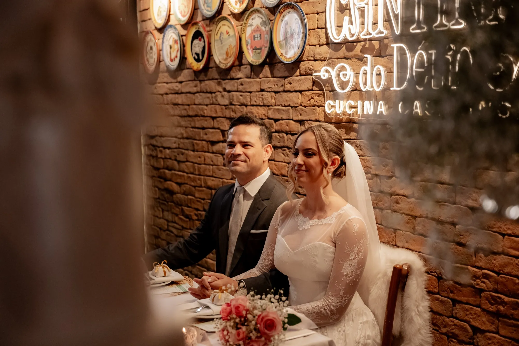 Os noivos Taiane e Juarez à mesa, diante do letreiro da Cantina